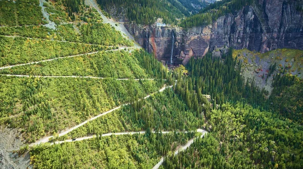 Piccola strada sterrata zig zagging su grande parete di montagna verso cascate su scogliere — Foto Stock