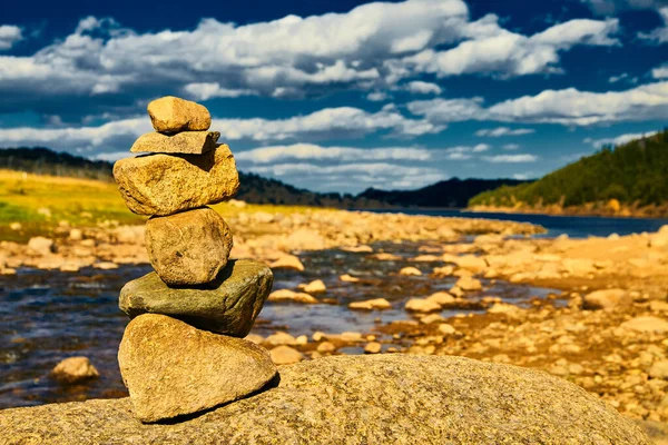 Stos kamieni Cairn w złocistym słońcu z tłem rzeki i gór — Zdjęcie stockowe