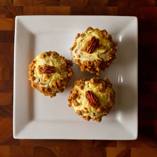 Fåglar syn på tre orange muffins toppad med glasyr och en pekan på en vit platta på ett bord — Stockfoto