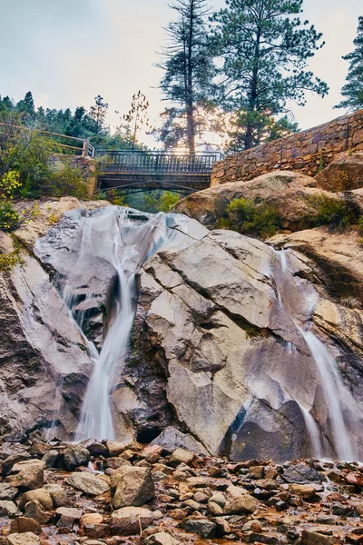 Cachoeira nas montanhas com ponte a pé e parede de pedra — Fotografia de Stock