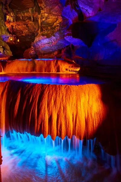 Cachoeiras em caverna subterrânea que flui sobre formações rochosas com luzes laranja e azul — Fotografia de Stock