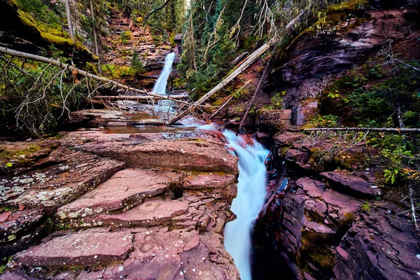 Вода бежит через глубокое ущелье с красными скалами и водопадом на заднем плане — стоковое фото