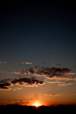 Karanlık gece gökyüzü ve batan güneş tarafından aydınlatılan bulutlar.