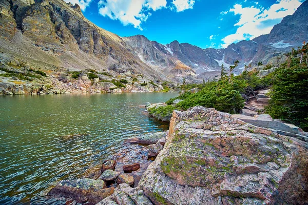 Зеленый лишайник на большом валуне, отдыхающий в озере в окружении гор — стоковое фото