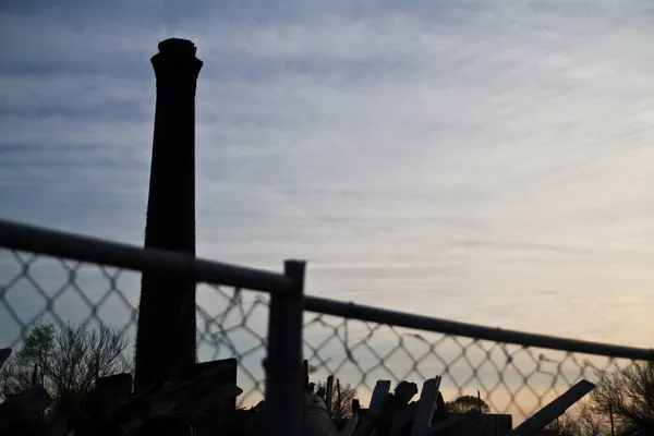 Des tours de fumée d'usine sur un ciel légèrement nuageux au-dessus d'une clôture à mailles de chaîne — Photo