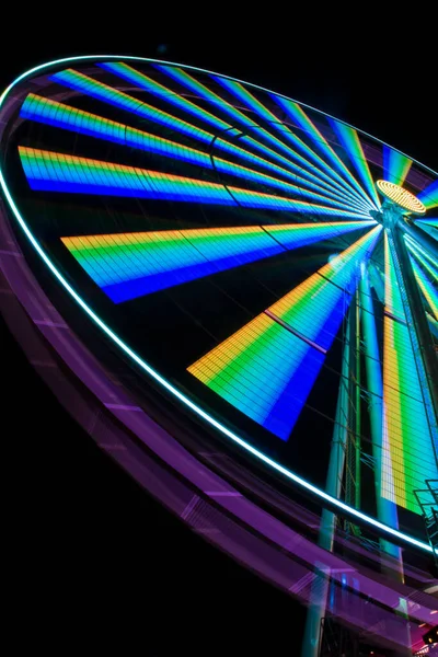 Worms eye view of a ferris wheel lit up at night with yellows greens blues and blacks — Stock Photo, Image