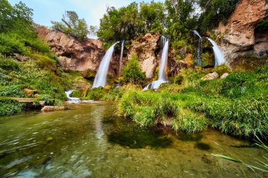 Nehirli yemyeşil bir arazi ve üç şelale kayalıklardan aşağı akıyor.