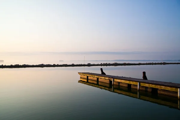 Длинный деревянный пирс простирается в спокойное озеро в ясный день — стоковое фото