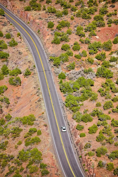 Visão para baixo da estrada curvando através do deserto aberto com carro branco — Fotografia de Stock