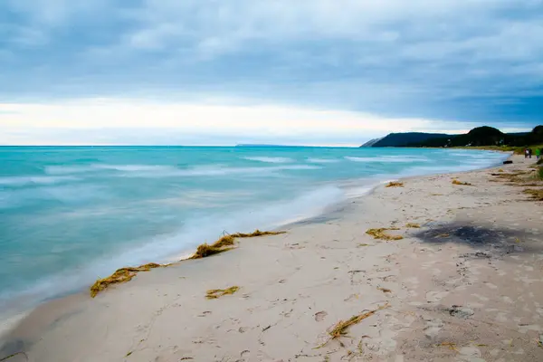 Чистая голубая вода смывается на легком песчаном пляже с облачным небом — стоковое фото