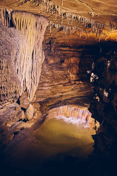 Cachoeira em caverna subterrânea ao lado de formações rochosas estalagmites e estalactites — Fotografia de Stock