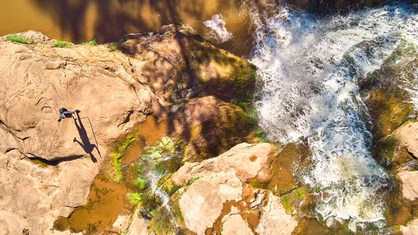 Escursionista dall'alto con lunga ombra di figura su rocce marroni accanto a cascate bianche — Foto Stock