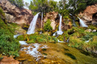 Üç şelale kayalıklardan nehre dökülüyor yemyeşil bitkilerle.