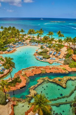 Işın havuzlu, yüzme havuzlu, palmiye ağaçlı ve okyanuslu tatil köyü balkonundan manzara