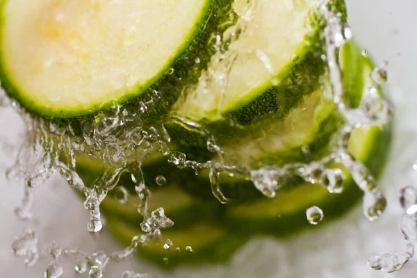 Cucumber slices stacked vertically splashed with water on a white background — Stock Photo, Image