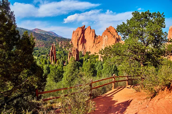 Ahşap çitli yürüyüş yolu ve daha büyük kırmızı kaya sütunlarının çöl manzarası.
