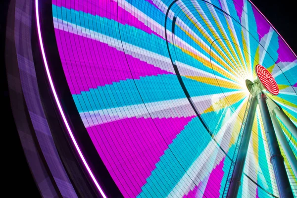 Ferris wheel fully lit up at night with pinks and blues and grays in a compass like design — Stock Photo, Image