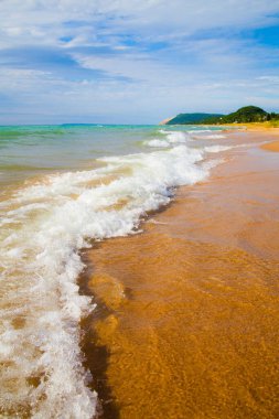 Beyaz köpüklü dalgalar kumlu bir sahilde tepeye çıkar.