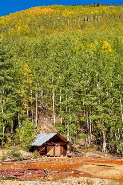 Liten övergiven hydda vid basen av stor kulle täckt av grönt och gult fall asp träd — Stockfoto