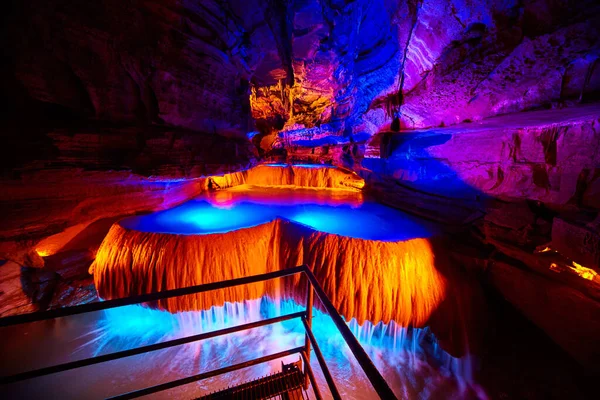 Grande cachoeira subterrânea na caverna no caminho do passeio com luzes laranja e azul — Fotografia de Stock