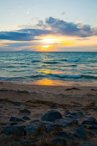 Zachód słońca zasłonięty niebieskimi chmurami nad falującymi falami i plażą — Zdjęcie stockowe