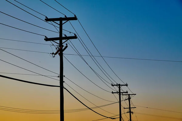 As linhas de energia estendem-se para a distância, silhueta pelo pôr-do-sol laranja — Fotografia de Stock