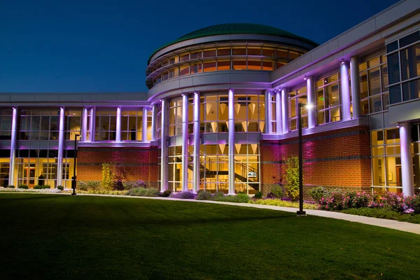 Přední dveře moderní budovy s mnoha okny za soumraku osvětlené fialové — Stock fotografie