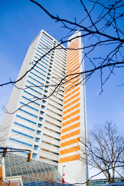 Um arranha-céu alto que é meio azul e meio laranja no inverno em um céu azul claro — Fotografia de Stock