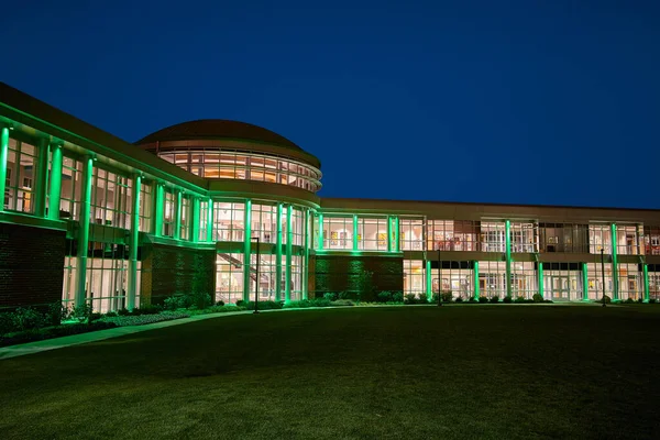 Přední pohled na kolej na univerzitě se zeleným osvětlením fasády a spoustou oken v noci — Stock fotografie