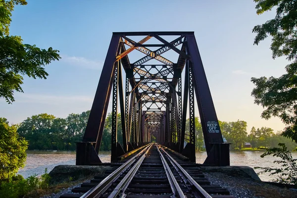 Перспективное движение металлического моста, ведущего через мост с железнодорожными путями в ясный день в окружении деревьев — стоковое фото