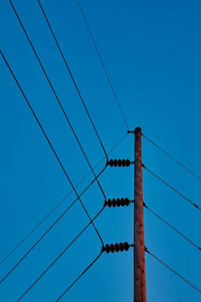 Les lignes électriques se fixent et se déroutent sur un poteau téléphonique par une journée de ciel bleu clair — Photo