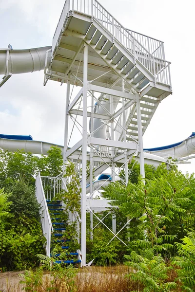 Shot of the base of a staircase overgrown with greenery and shrubs leading up to a water slide — Stock Photo, Image