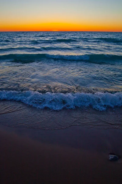 Fale płyną do piaszczystego brzegu o zachodzie słońca. — Zdjęcie stockowe