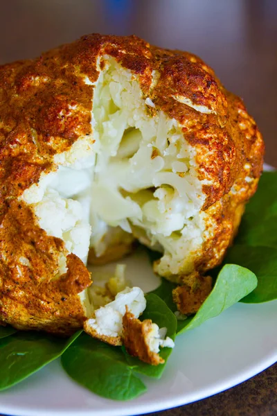 Cross section of a seasoned and cooked head of cauliflower on a bed of greens — Stock Photo, Image
