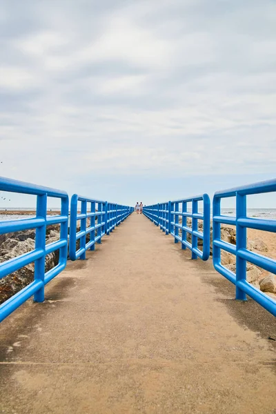 Cement walkway on beach with metal blue railing and walkers in distance — Stock Photo, Image