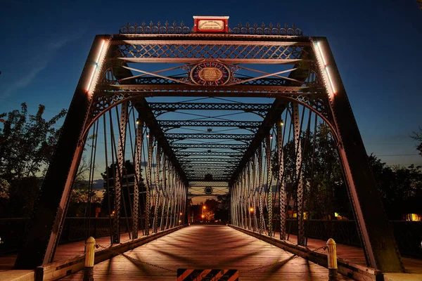 Puente de metal que conduce al centro iluminado por la luz de la calle al atardecer —  Fotos de Stock