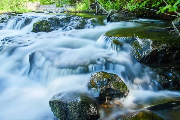 Vue rapprochée des cascades lisses sur des roches mousseuses humides avec barrage en arrière-plan — Photo