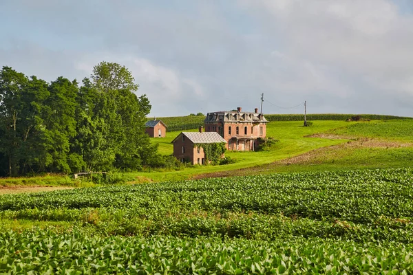 Paisagem tiro de uma mansão de tijolo vermelho de uma distância com terras verdes em primeiro plano e uma floresta no meio do solo — Fotografia de Stock