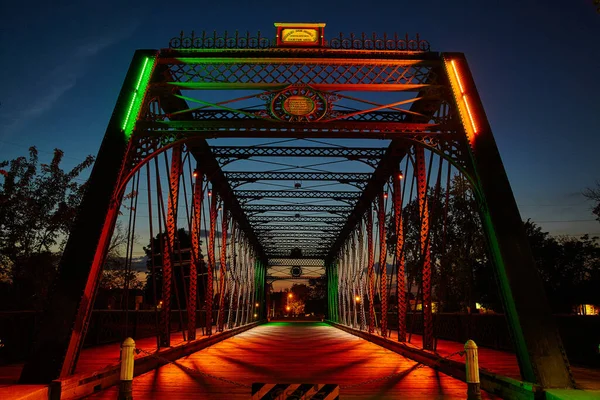 Ponte de metal que leva ao centro da cidade iluminado com luzes laranja e verde multicoloridas ao entardecer — Fotografia de Stock