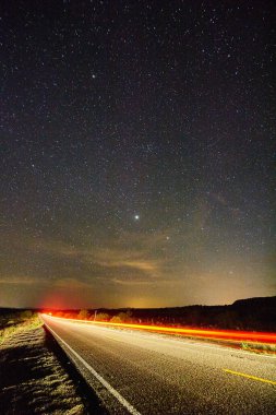 Çölün ortasında, üzerinde yıldızlı bir gökyüzü olan terk edilmiş bir yoldaki trafiğin zaman aşımına uğramış görüntüsü.