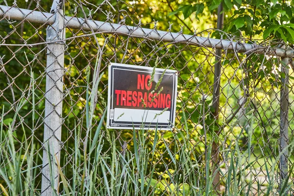 No trespassing sign in red text on metal fence in forest — Stock Photo, Image