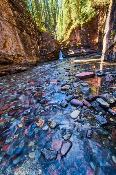 Rivier van kleine kleurrijke rotsen op de bodem van kloof met waterval in afstand — Stockfoto