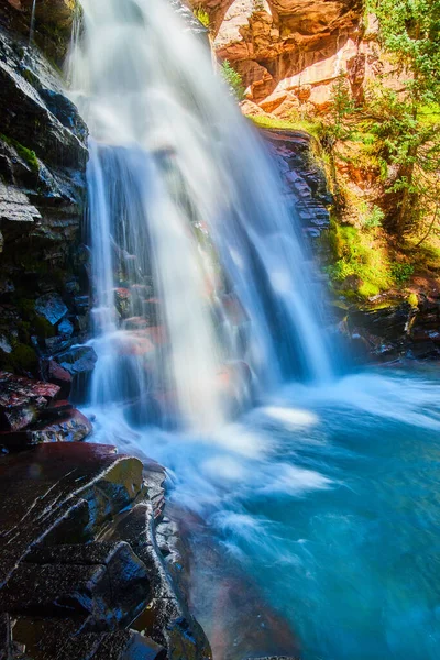 Dettaglio di cascata su scogliere con rocce rosse e muschio in secchio d'acqua blu — Foto Stock