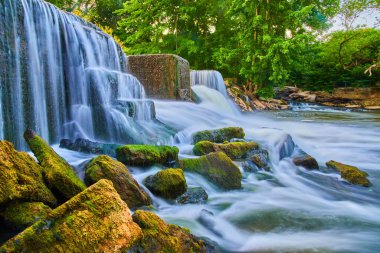İnsan yapımı şelaleler ve renkli yosunlu kayaların etrafında akan baraj.
