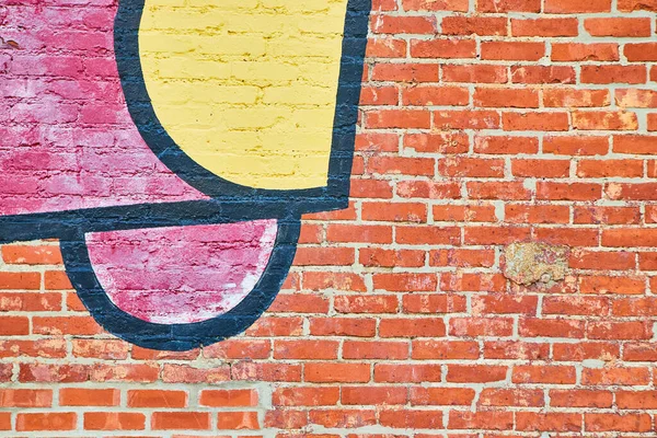 Wall of textured red brick up close with patch of red, black, and yellow graffiti — Stock Photo, Image