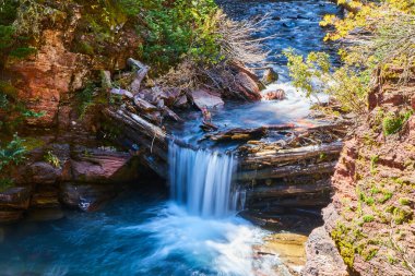 Kanyondaki kütüklerin üzerinden şelale akıyor.