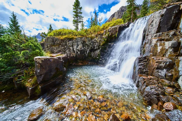 Величний водоспад у відро води, оточений камінням, вкритим барвистим лишайником — стокове фото
