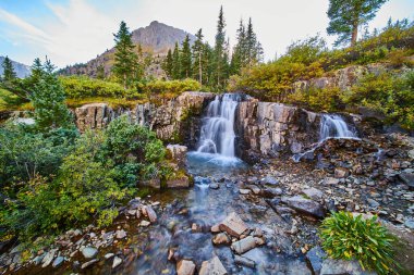 Güzel şelalelerin sığ nehir yatağının arka planında dağlar olan görüntüsü.