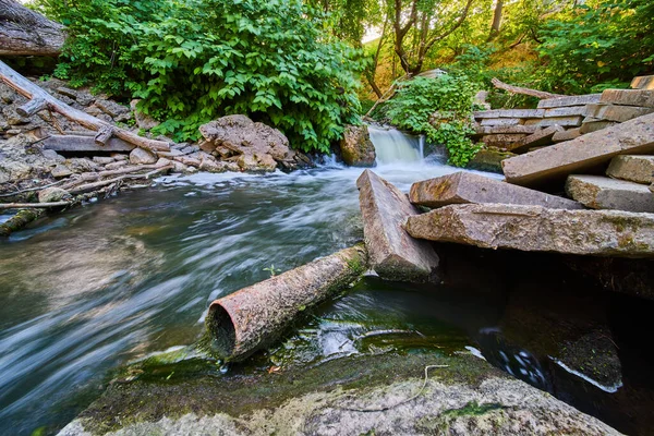 Metalen roestige pijp in rivier met puin en cement blokken door kleine waterval — Stockfoto