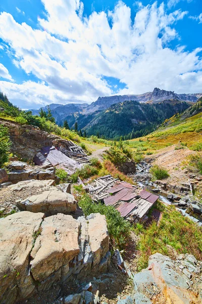 Vecchie capanne in metallo e legno distrutte accanto al fiume in una vasta valle e vista sulle montagne — Foto Stock